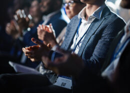 Close Up on Hands of a Crowd of People Clapping in Dark Conference Hall During a Motivational Keynote Presentation. Business Technology Summit Auditorium Room Full of Delegates.